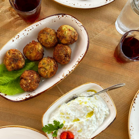 Goldbraune griechische Zucchini-Fritters mit cremigem Tzatziki, perfekt als Meze mit Minos natives Olivenöl extra.